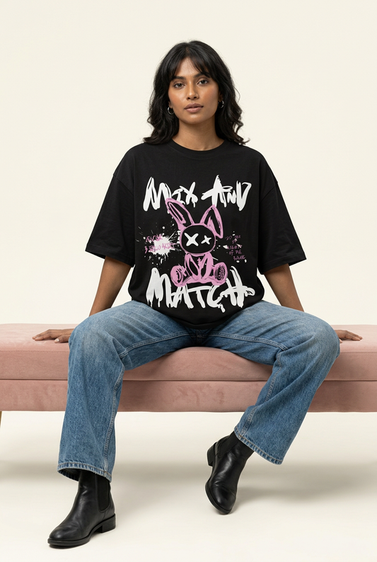 Pink graffiti rabbit oversized tee with loose blue jeans, seated pose